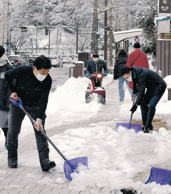 歩道に積もった雪をどかす人＝２１日午前７時５０分、金沢市本多町３丁目