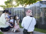 沖縄戦犠牲者の氏名が刻まれた「平和の礎」を訪れ、手を合わせる家族連れ＝２３日午前、沖縄県糸満市の平和祈念公園