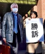 「勝訴」と書かれた紙を掲げる弁護士と原告の奥田恭正さん＝１８日午後、名古屋地裁前